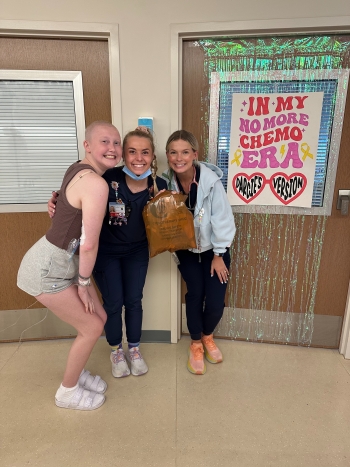 Darcie and nurses in front of No more chemo era poster on her door