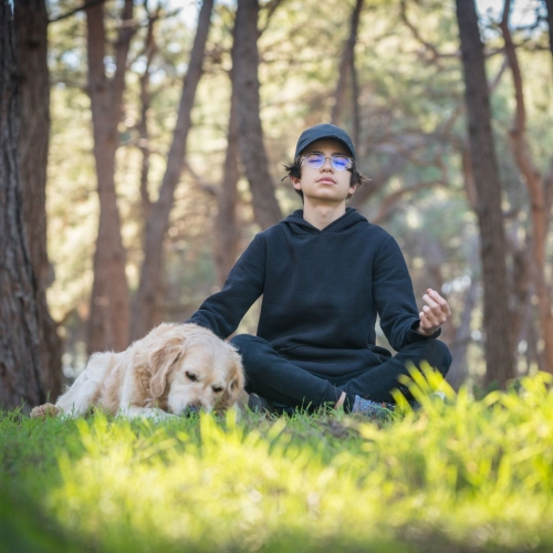 Teen boy meditating in woods with dog