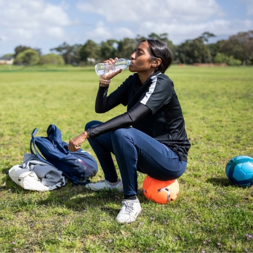 Teen girl resting on soccer ball drinking water