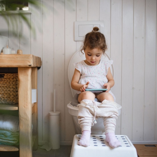 Little girl sitting on toilet with tablet