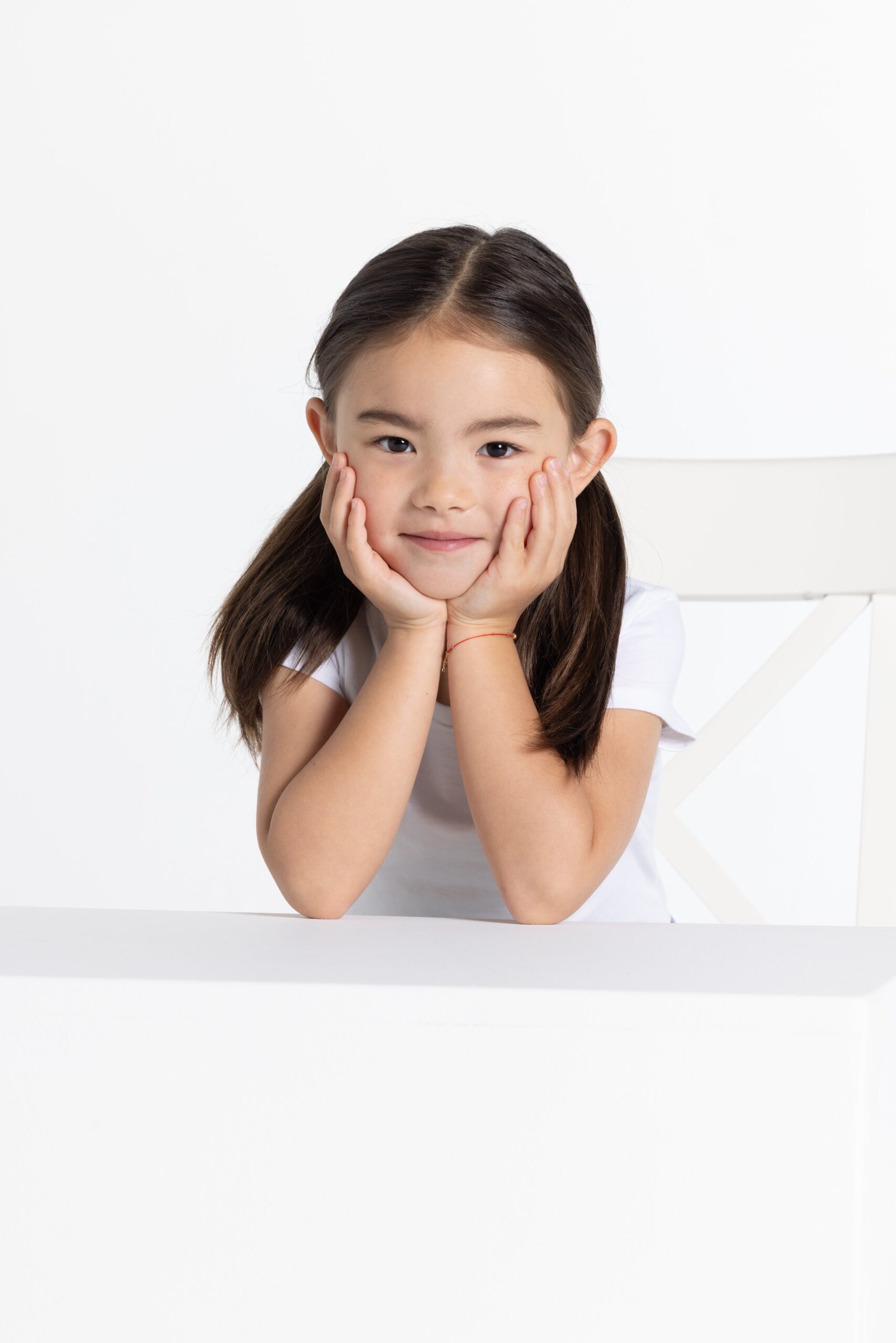 Child hold smiles while holding her head in her hands.
