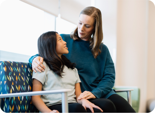 mom with arm around daughter sitting on colorful bench in hallway of Dayton Children's Hospital in Ohio