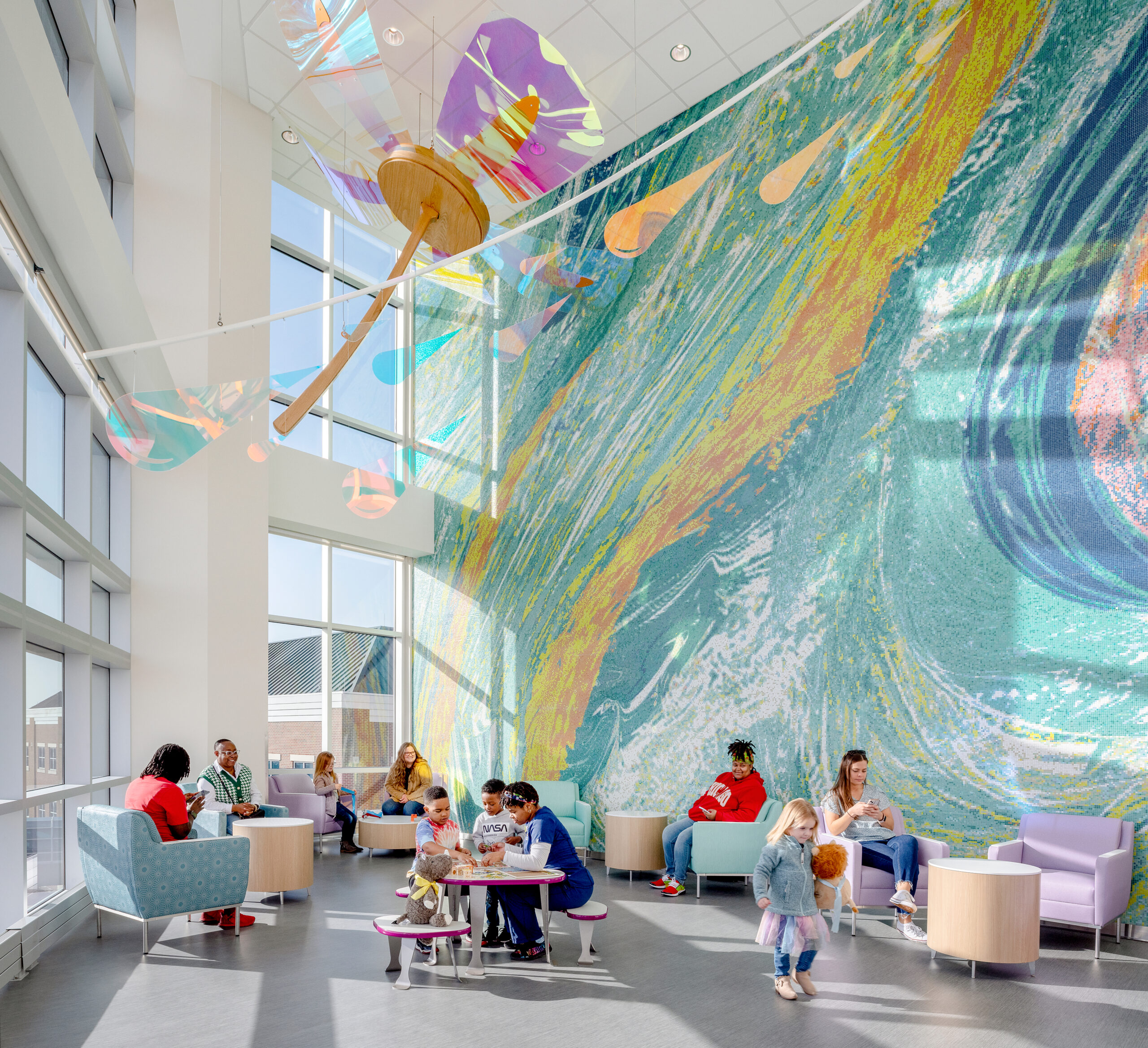 Families gather in a colorful hospital lobby with a large mural, showcasing the spaces and care made possible through donor support.