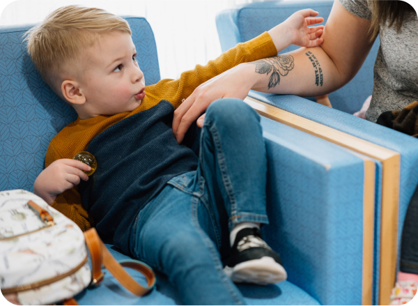 A young child sits in a chair next to caregiver in a bright, welcoming space at Dayton Children’s, representing trust, safety, and the mission behind every visit