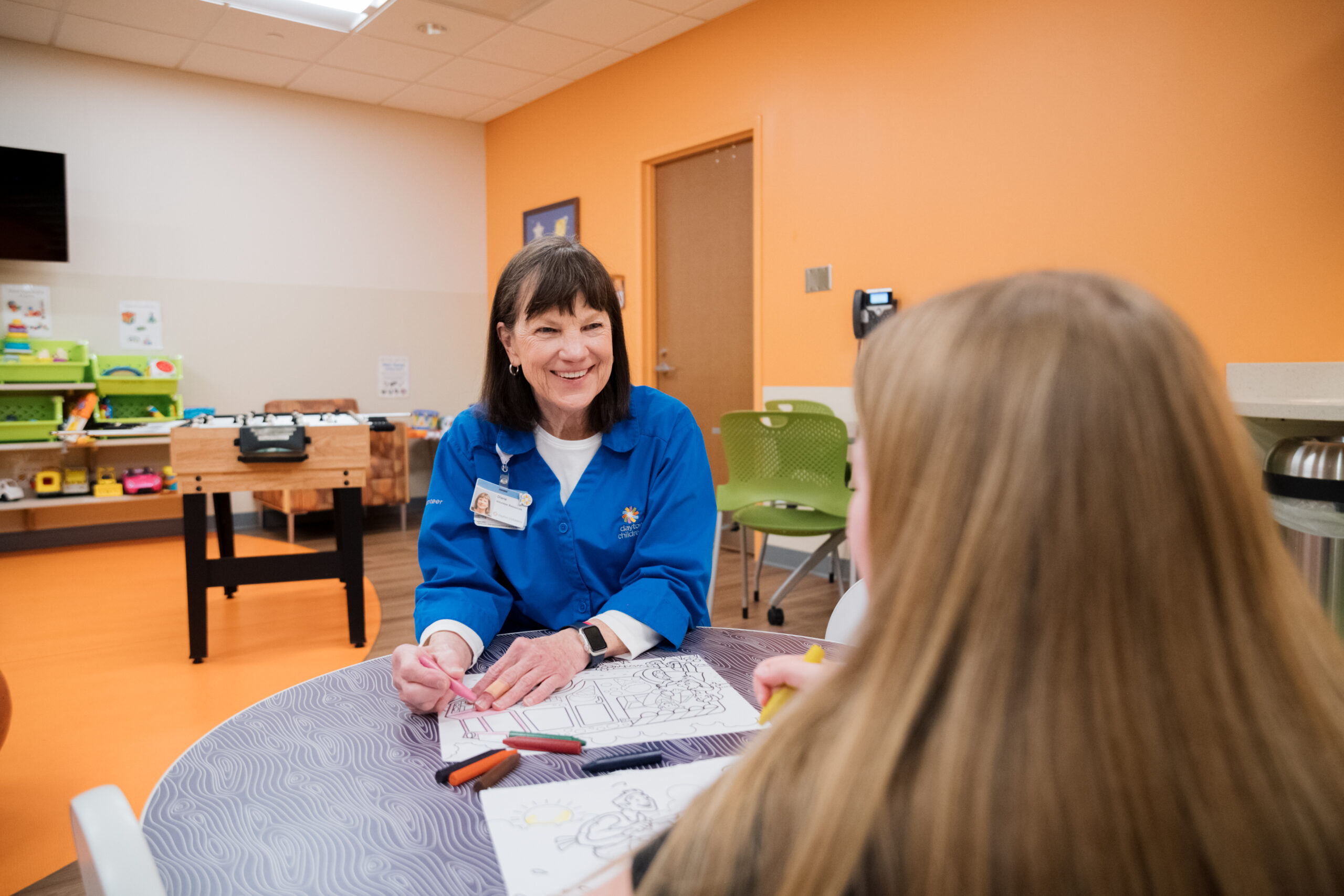Female volunteer coloring with a young girl patient in the hospital’s activity room.
