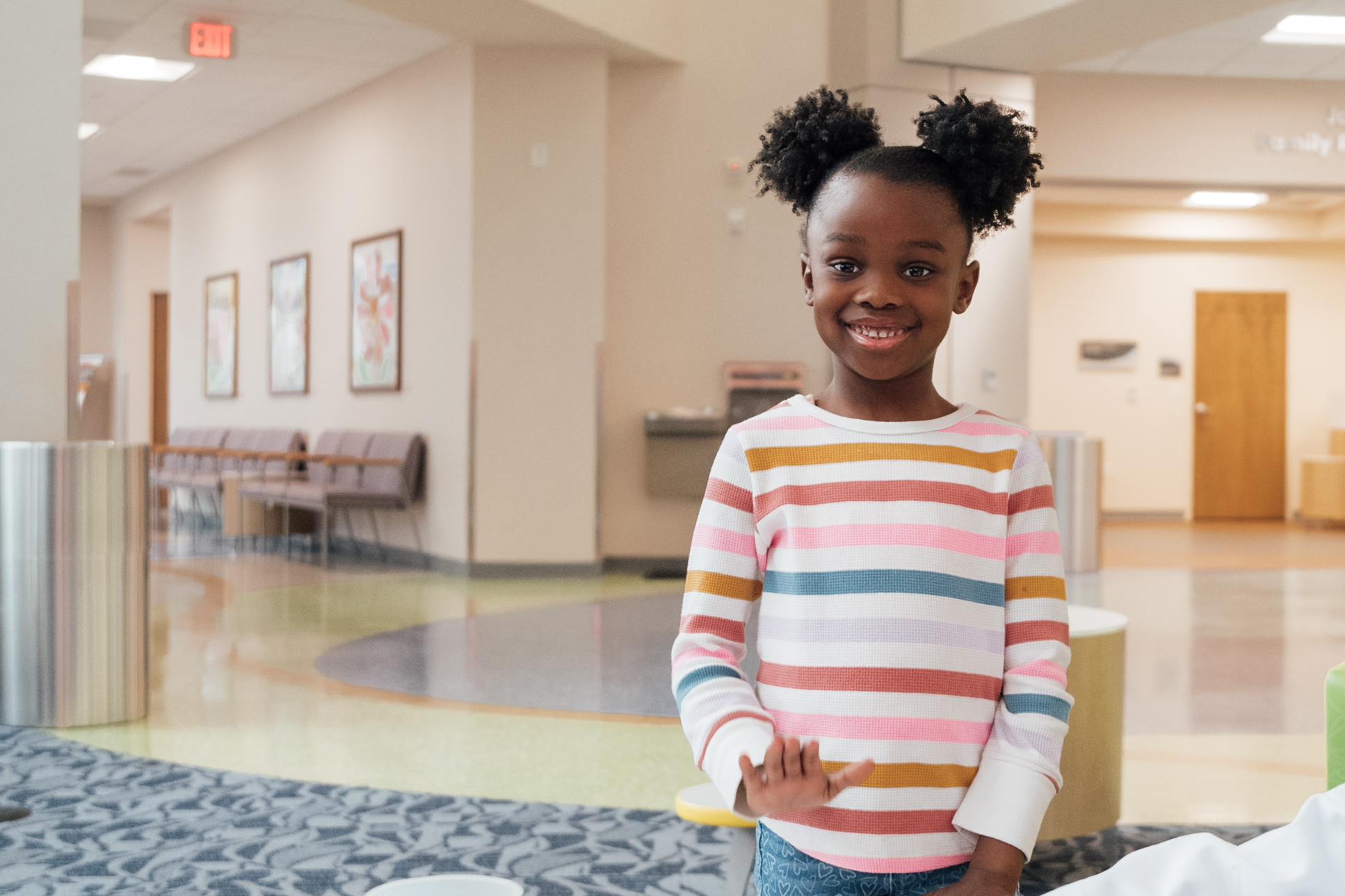 Cute young black girl with ponytails and a striped colorful sweater standing, smiling in the hallway of Dayton Children’s Hospital in Dayton, Ohio