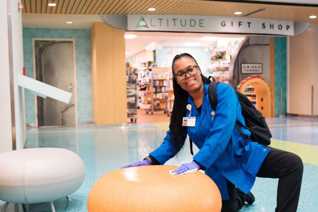 A hospital volunteer wipes down a table in a child-friendly space, representing behind-the-scenes contributions to a clean, welcoming care environment.