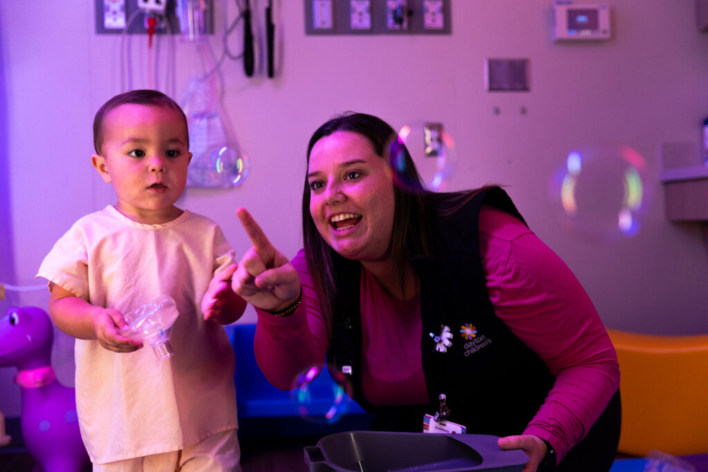 Dayton Children's Hospital patient playing with bubbles alongside a Dayton staff member in a colorful playroom