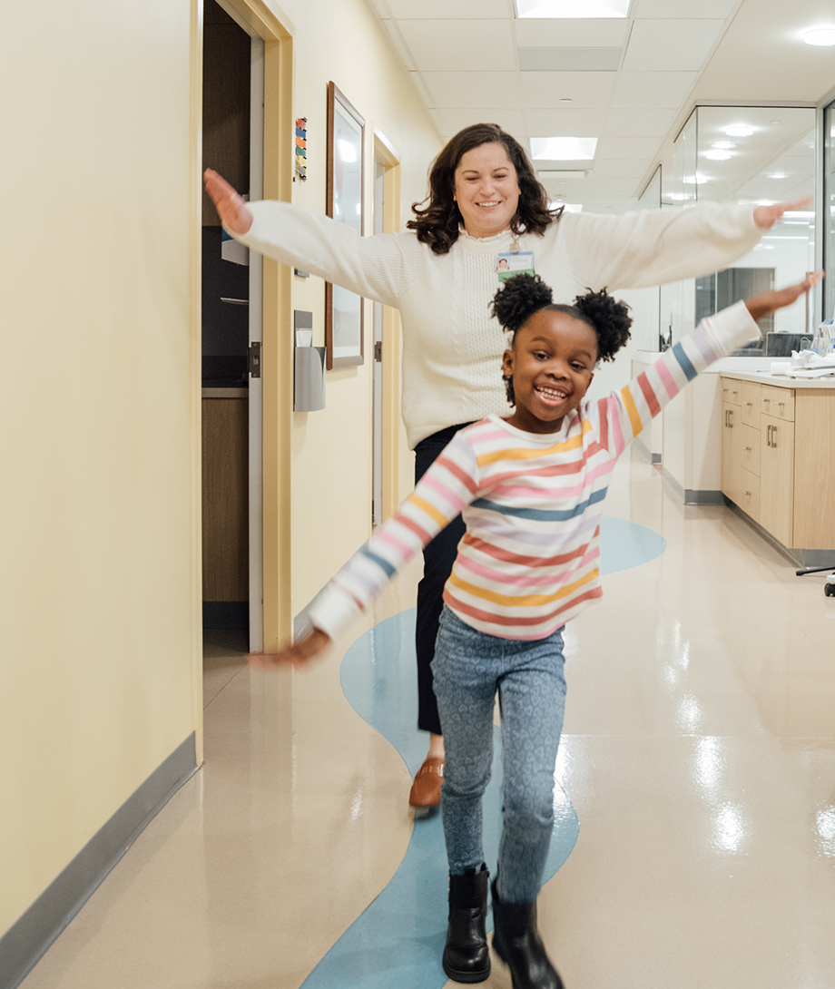 young patient and provider smile waving arms like an airplane in clinic hallway