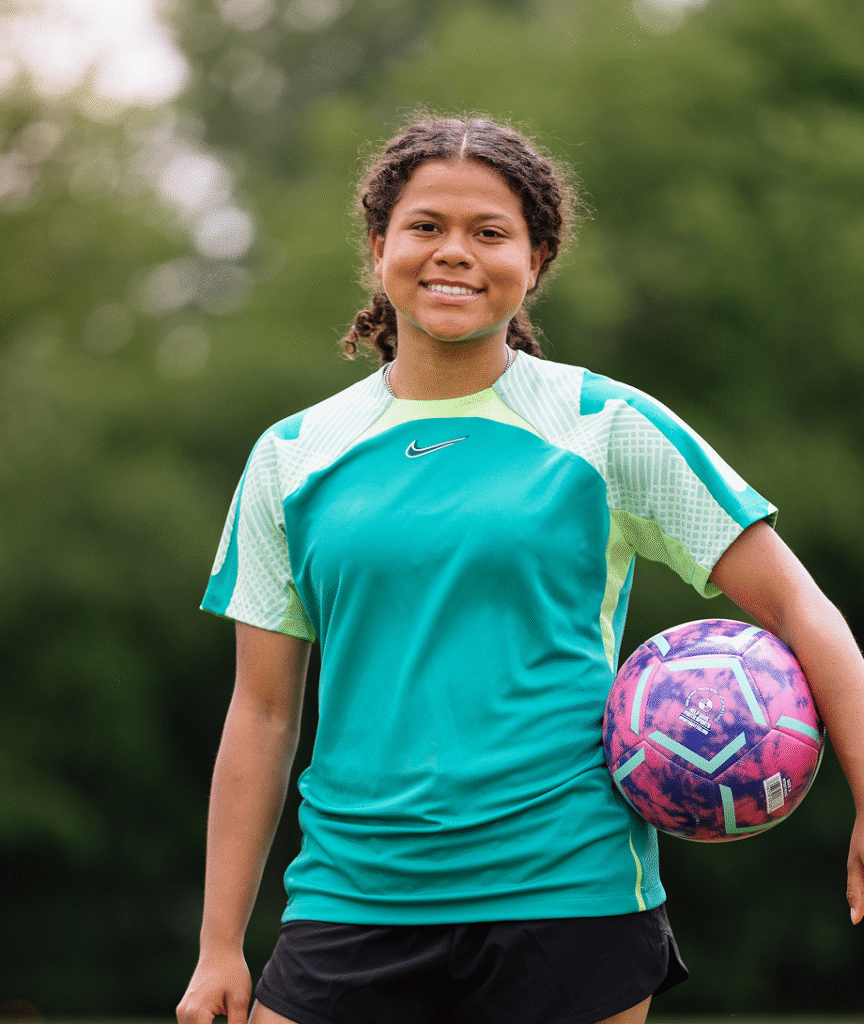 Smiling girl holding a ball under her arm.
