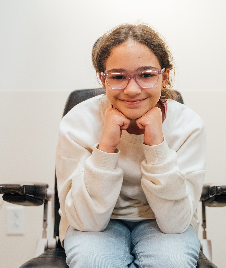 Smiling young patient in a wheelchair at Dayton Children’s Hospital, seated confidently with hands under chin.