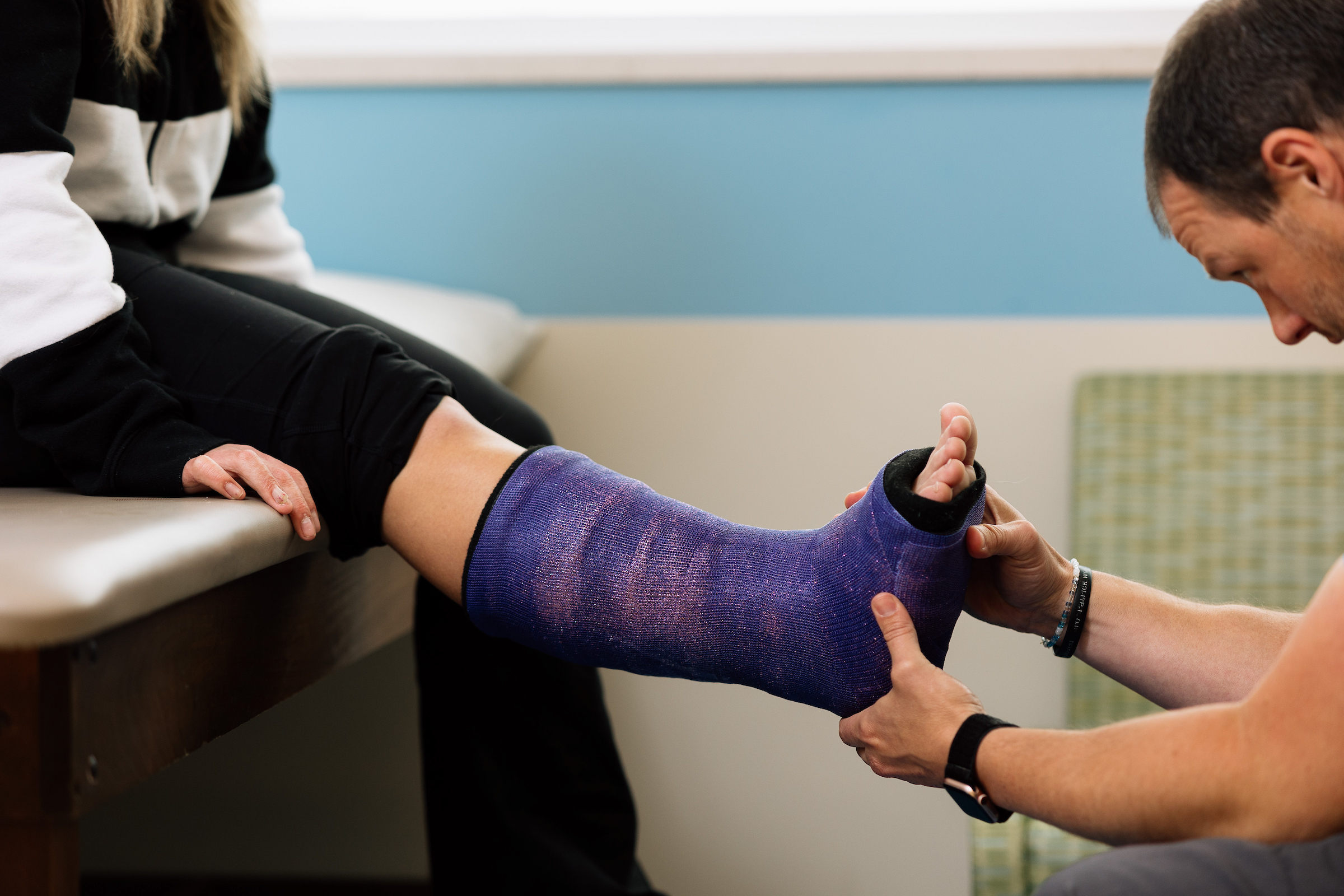 A medical professional is holding and examining a patient's leg, which is in a purple cast for a fracture. 
