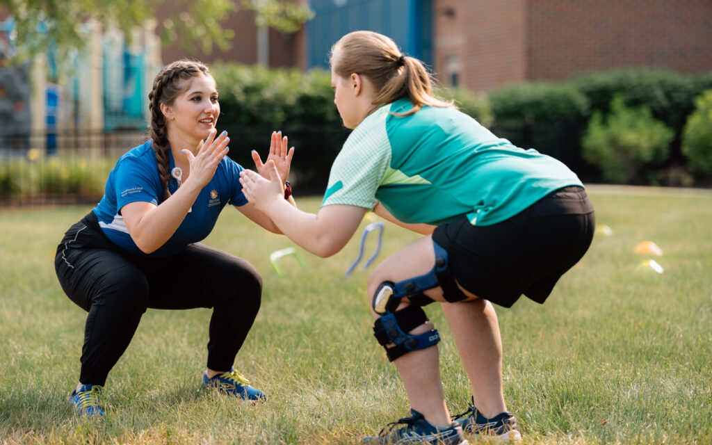teenage girl bending down while practicing sports medicine with her provider across from her