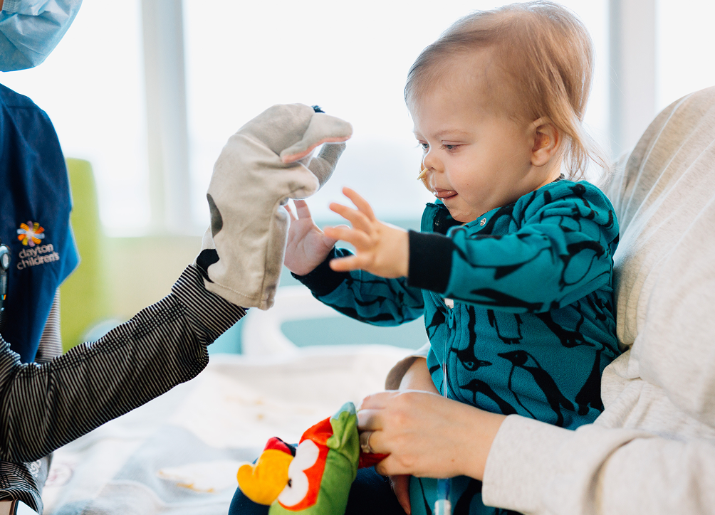 Toddler smiling while interacting with a hand puppet during a community activity.
