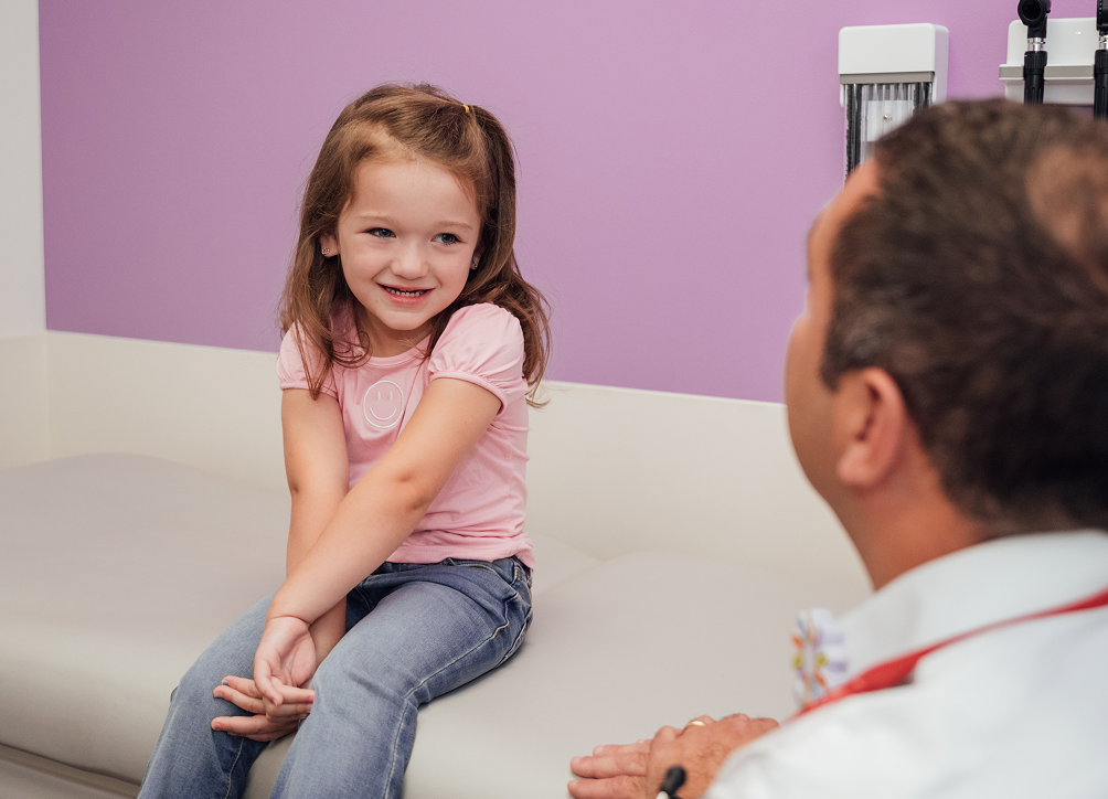 Smiling young patient sitting on an exam table with a doctor at Dayton Children’s Hospital.