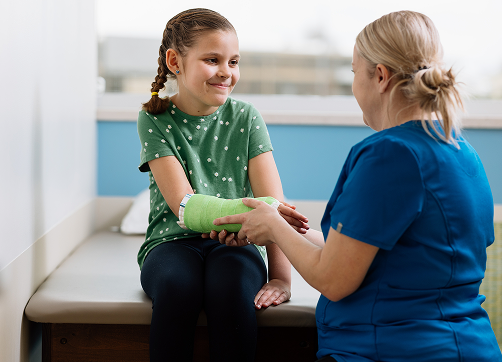 Female nurse holding young female patient’s fractured arm in a green cast 
