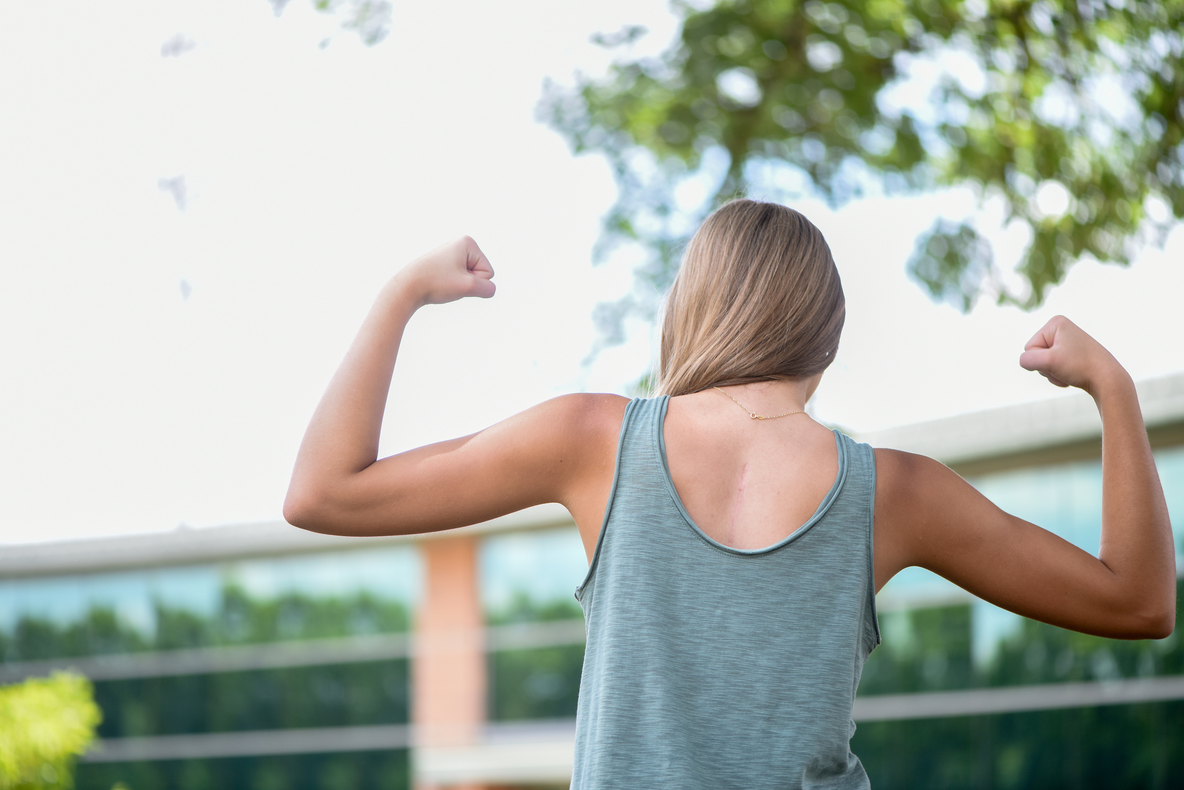 A girl is standing with her back to the camera, flexing her biceps. 