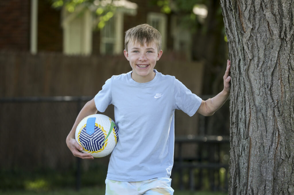 young boy holding  a soccer ball after recovery from sports medicine services