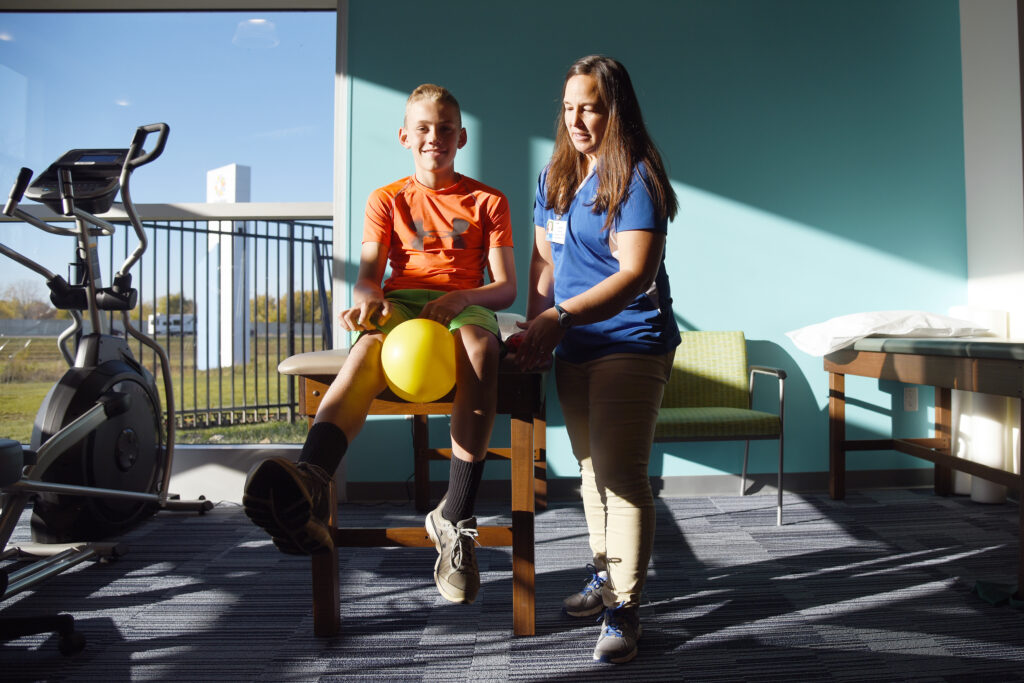 young boy participating in sports medicine session while sitting on a table next to a pediatric provider