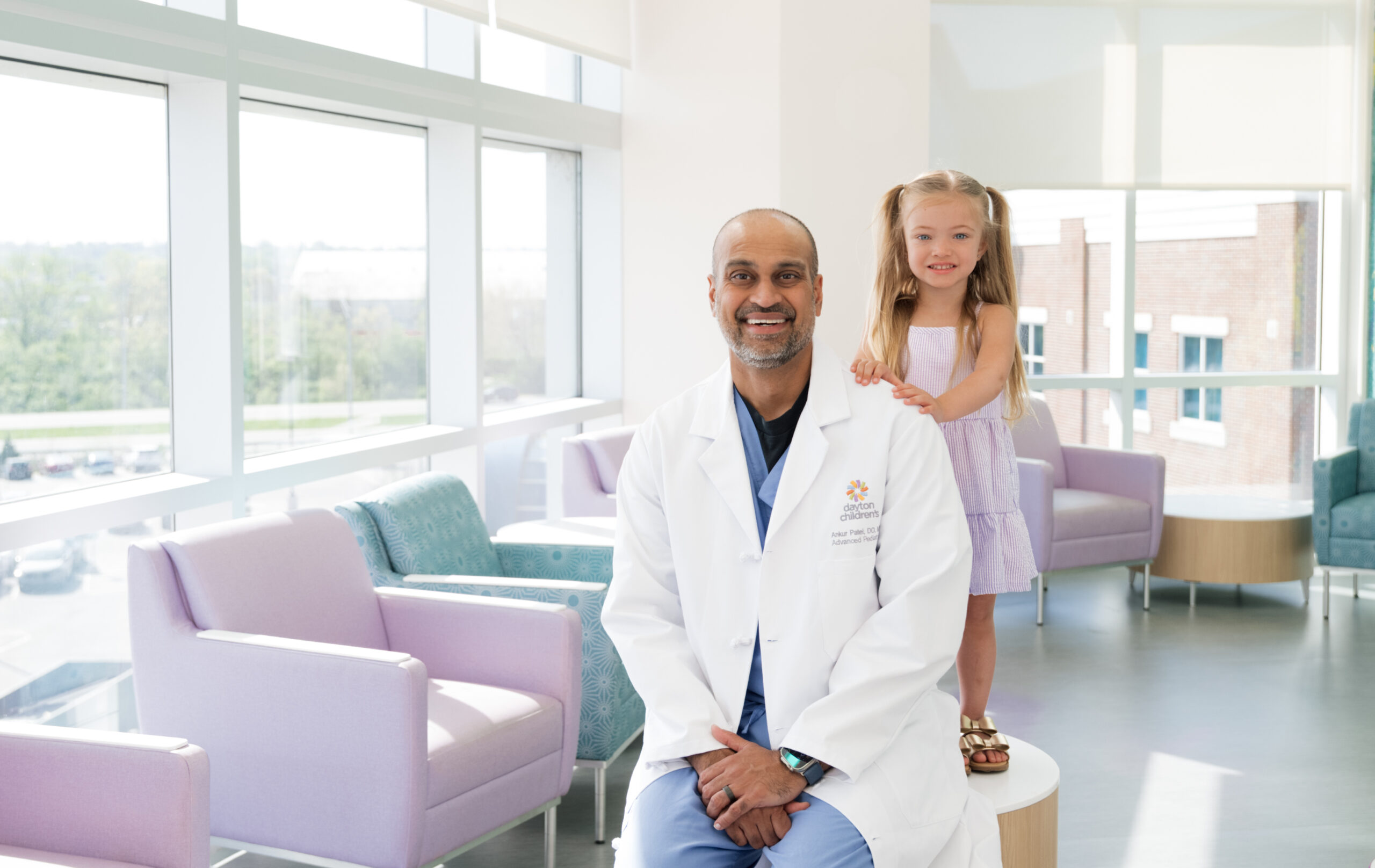 Male ENT provider sitting in front of a standing girl patient in a hospital waiting room.