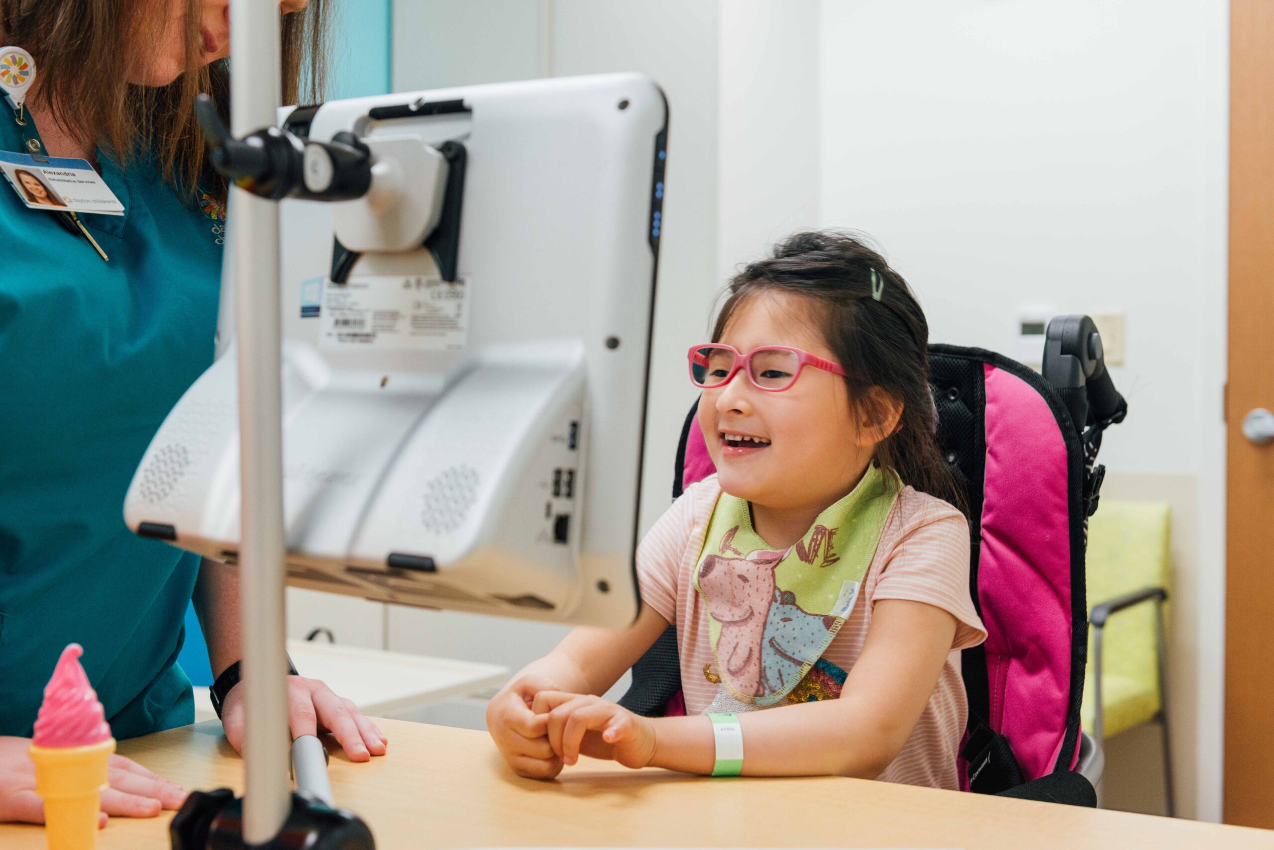 A young nonverbal girl works with a rehab specialist to communicate through a computer screen.