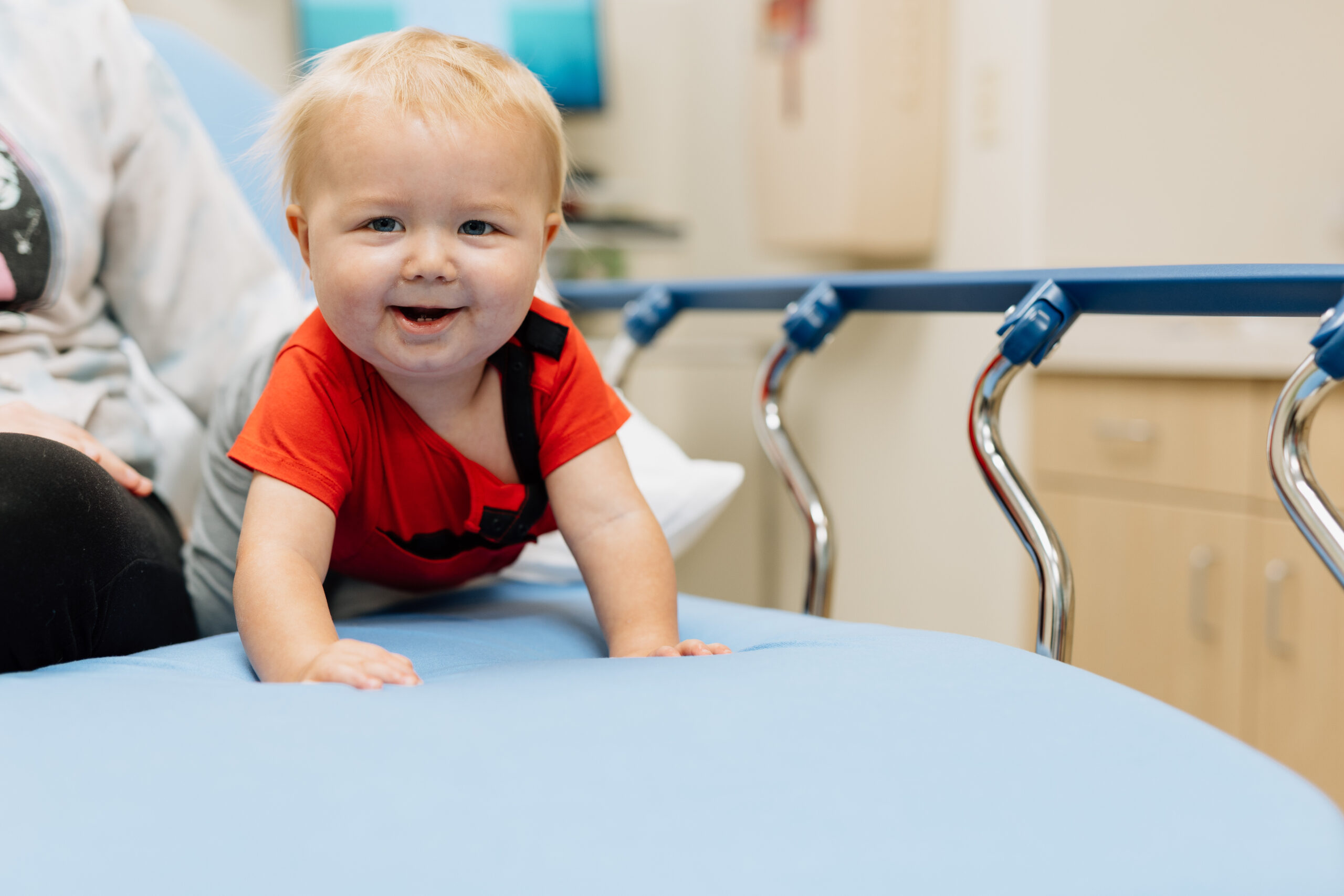 Happy baby sitting on a hospital bed, smiling at the camera.