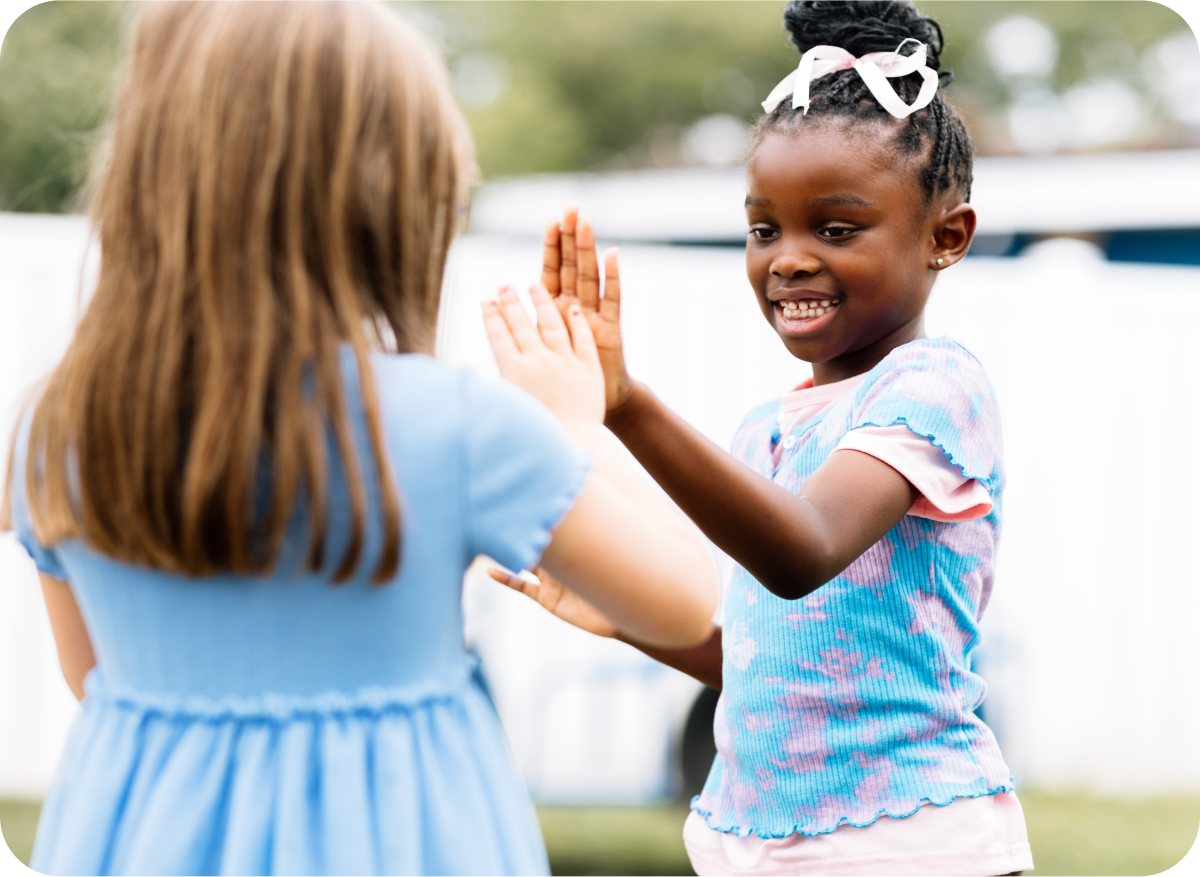 Two young girls smiling and high-fiving outdoors during a community health event at Dayton Children’s Hospital
