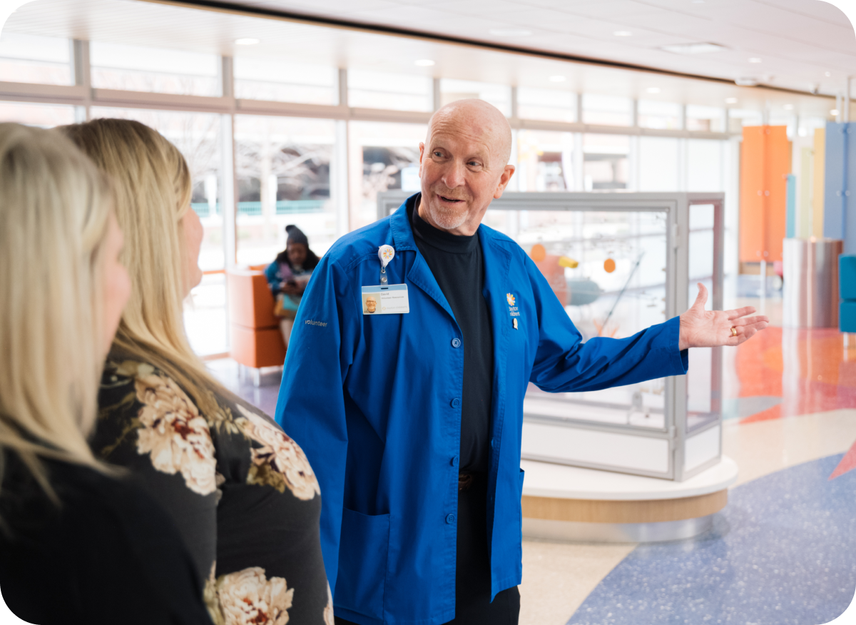 Hospital volunteer in a blue coat welcoming a visitor at Dayton Children’s Hospital lobby