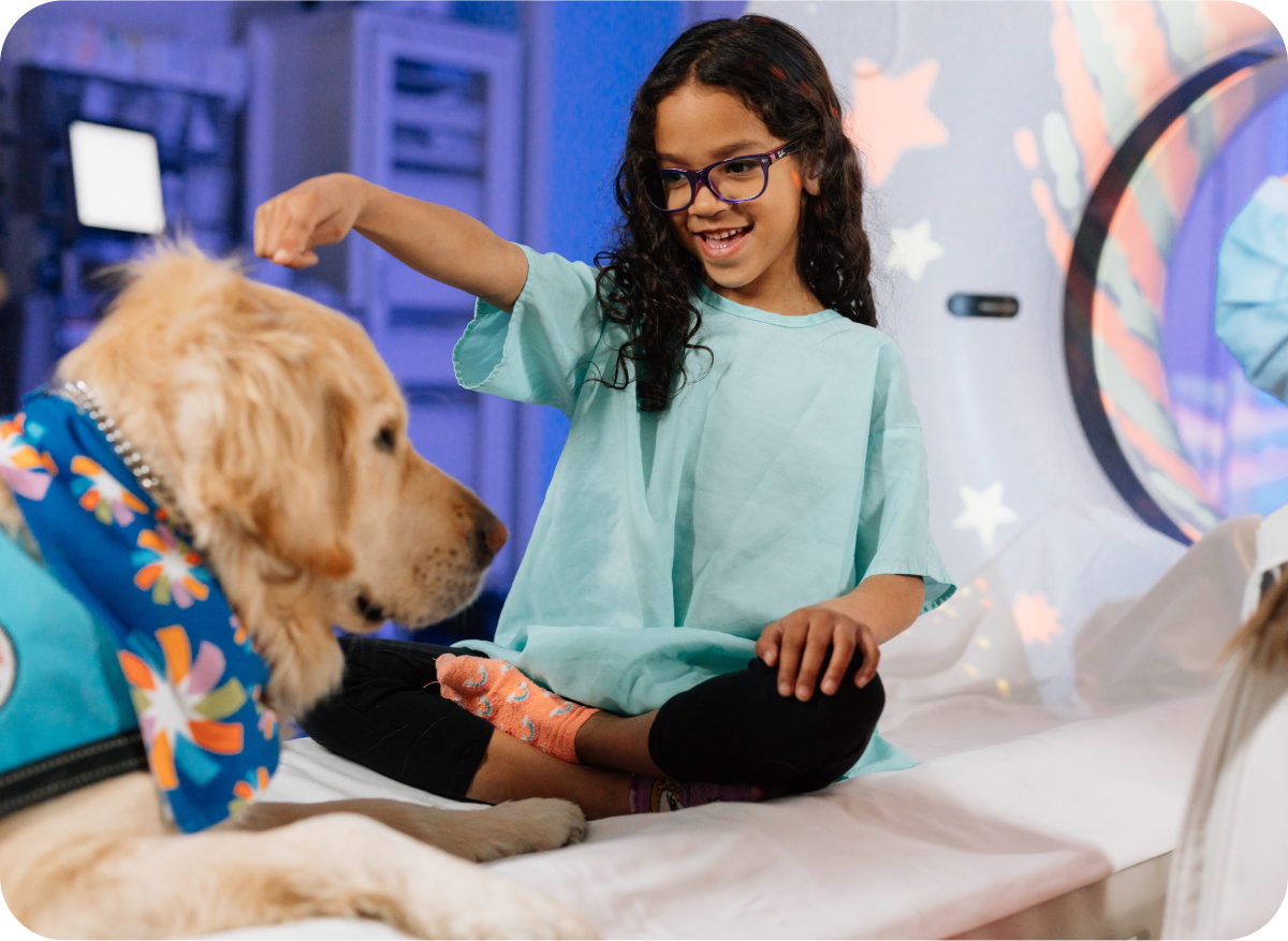Young patient smiling and reaching out to a therapy dog dressed in a colorful bandana.