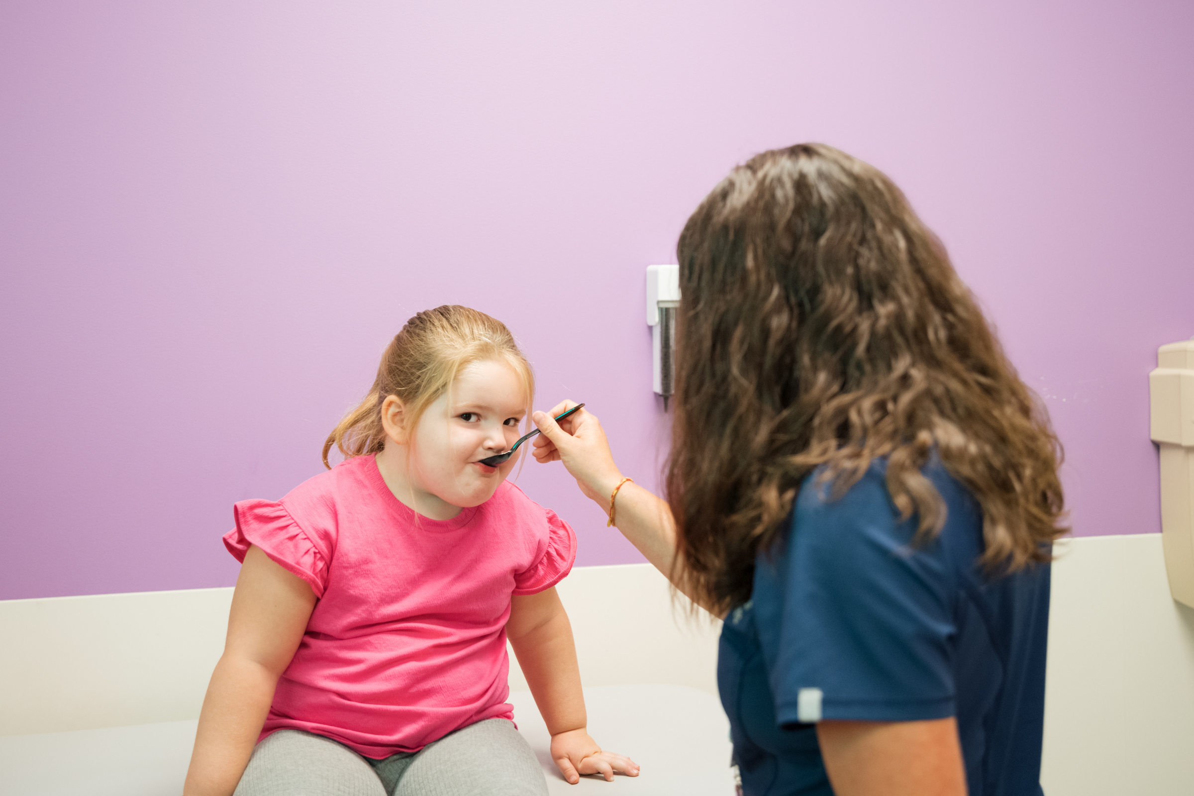 Young girl is fed peanut butter on a spoon by female nurse for food allergy testing and evaluation