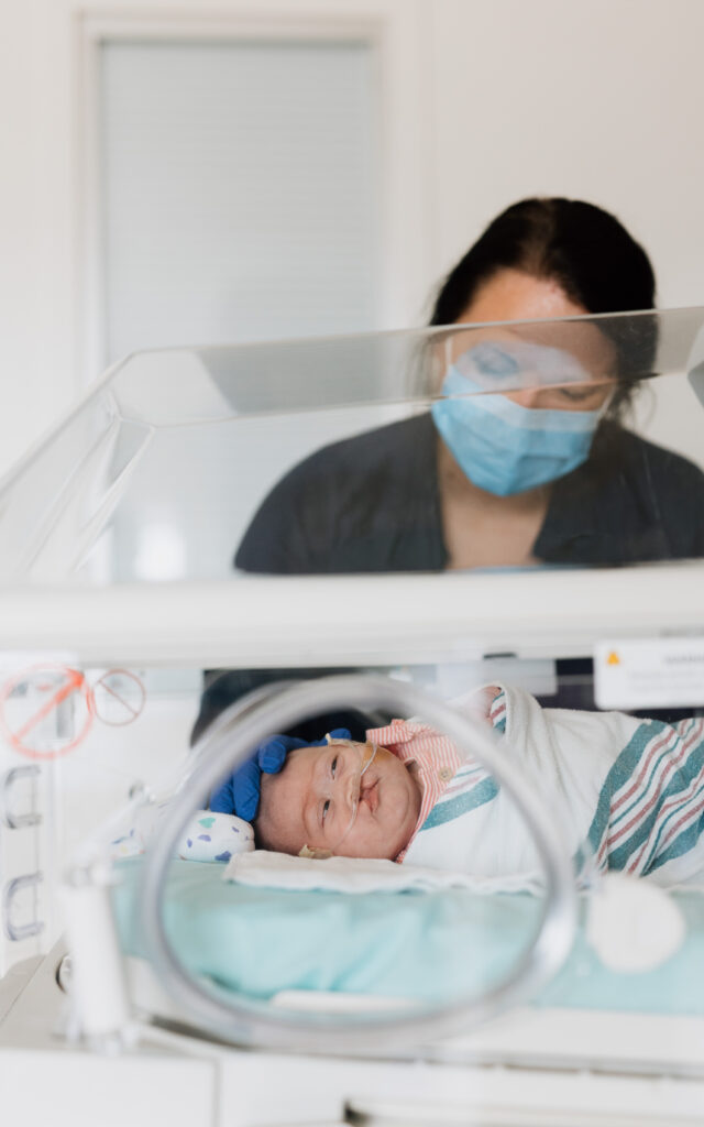 A baby in a NICU bed with an oxygen tube being monitored by a Dayton Children’s staff member.