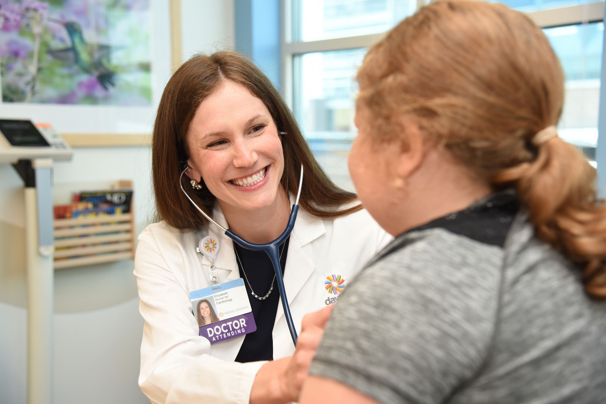 Female pediatric cardiologist listening to young girls heart with a stethoscope while in bright clinic room