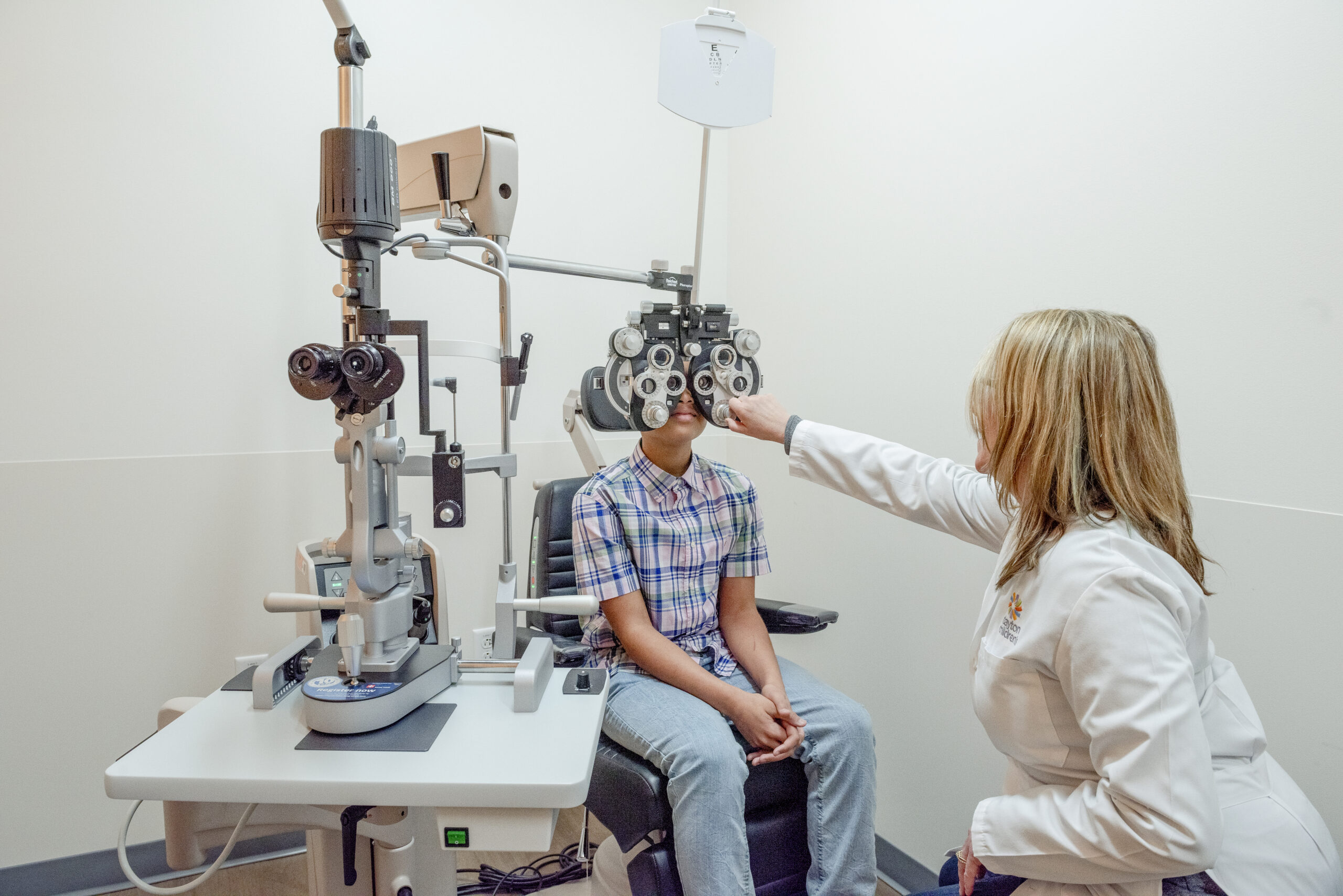 An ophthalmologist tests a teen boy's eyesight with a refractor/phoropter.