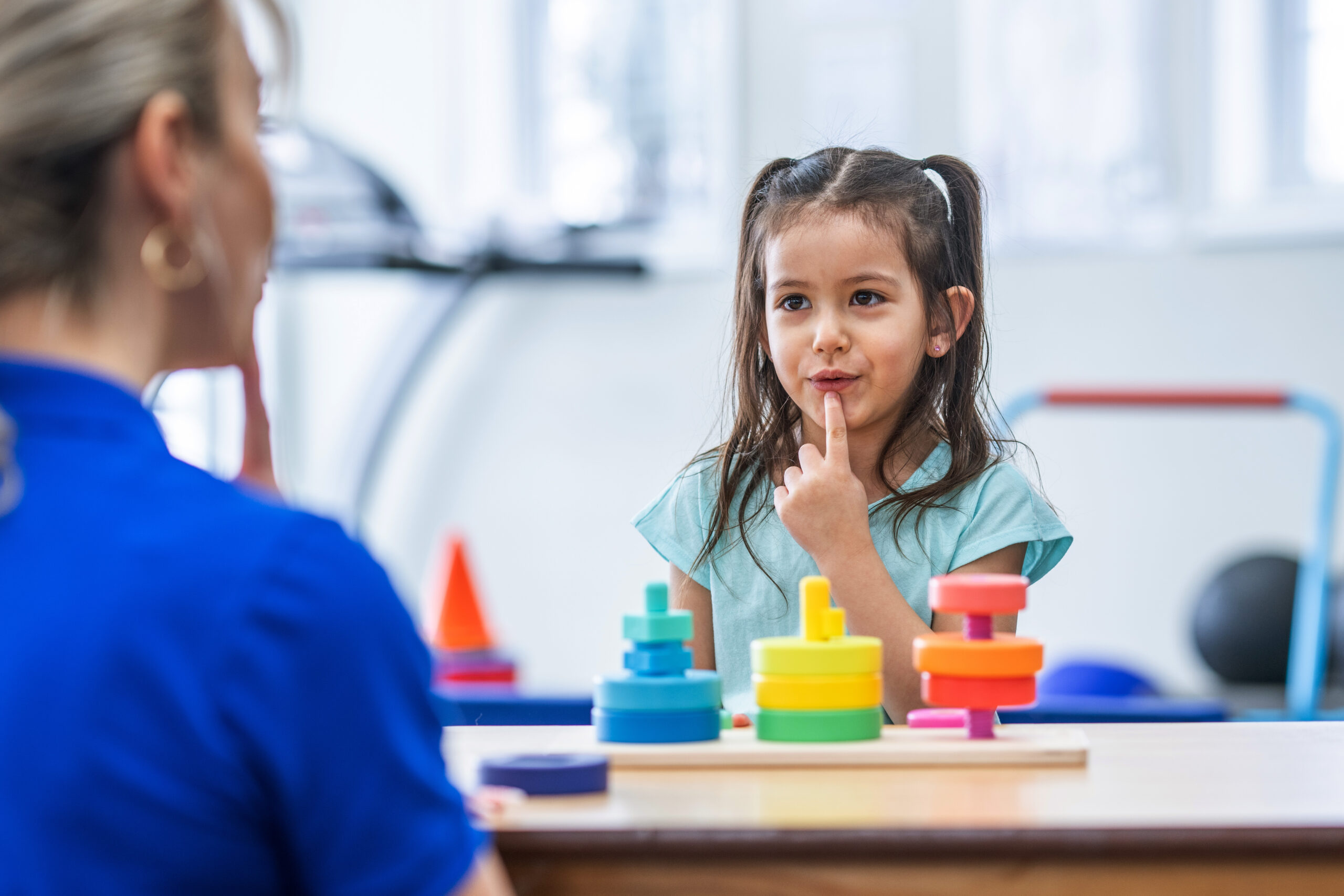 A young girl works with a speech therapist to mimic the sounds the therapist is making and seeing how different words change the shape of her mouth. 