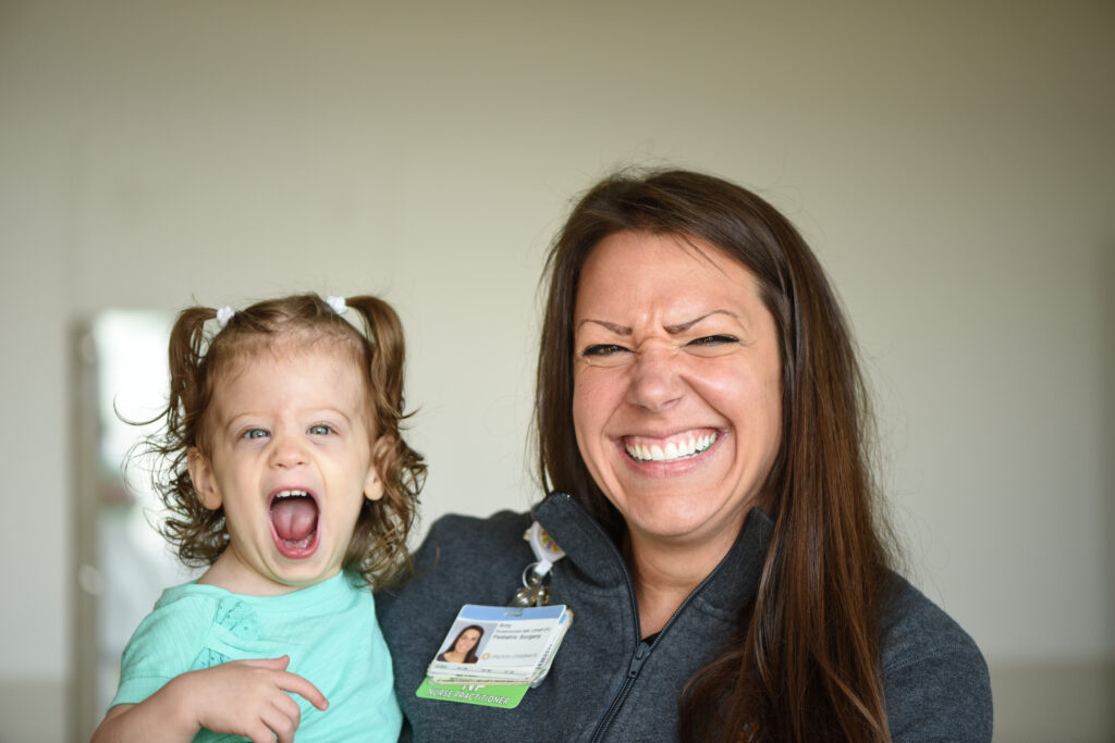 A smiling little girl laughing with her nurse and looking at the camera.