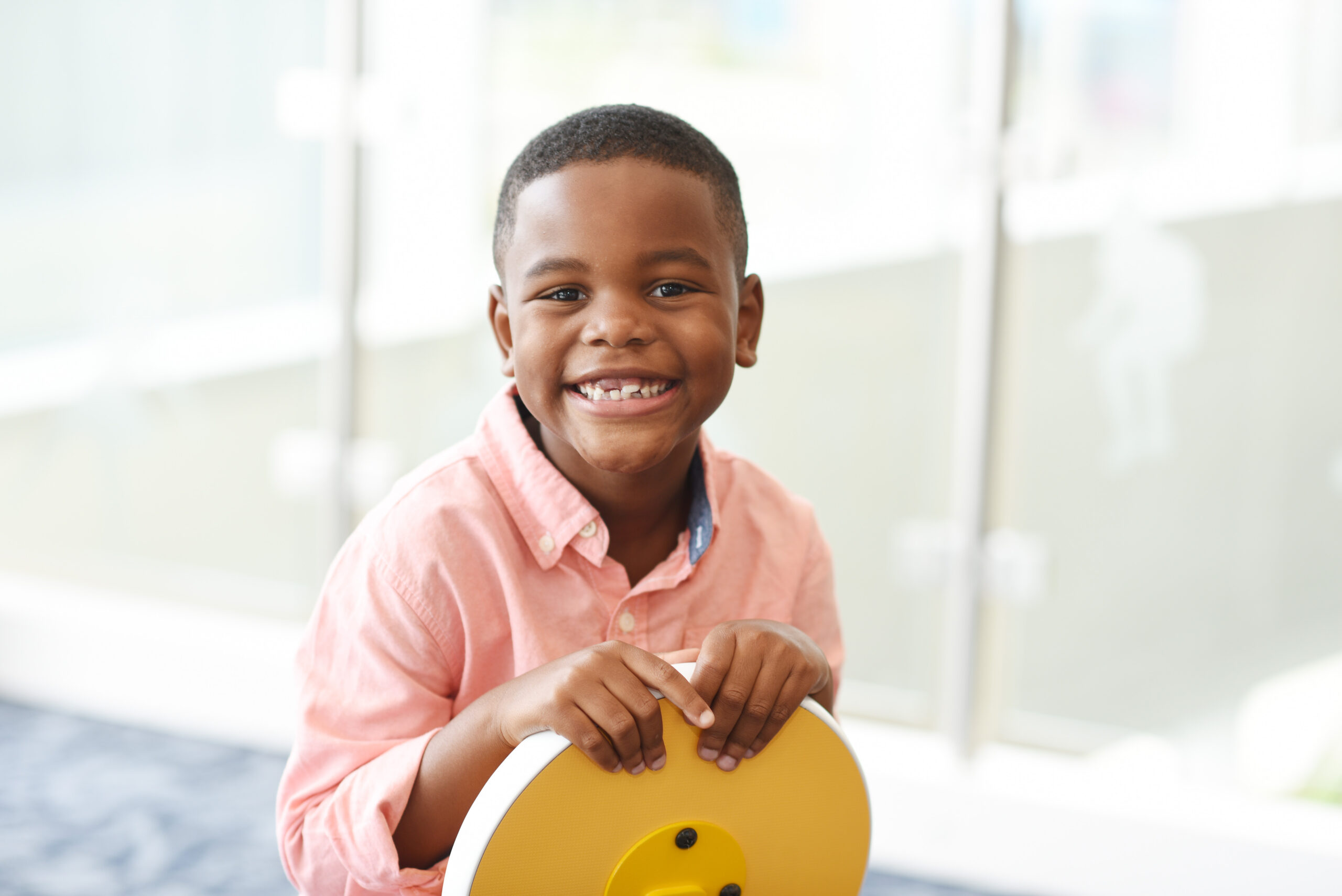 A little boy, sitting in a yellow chair backwards, looking at the camera and smiling.