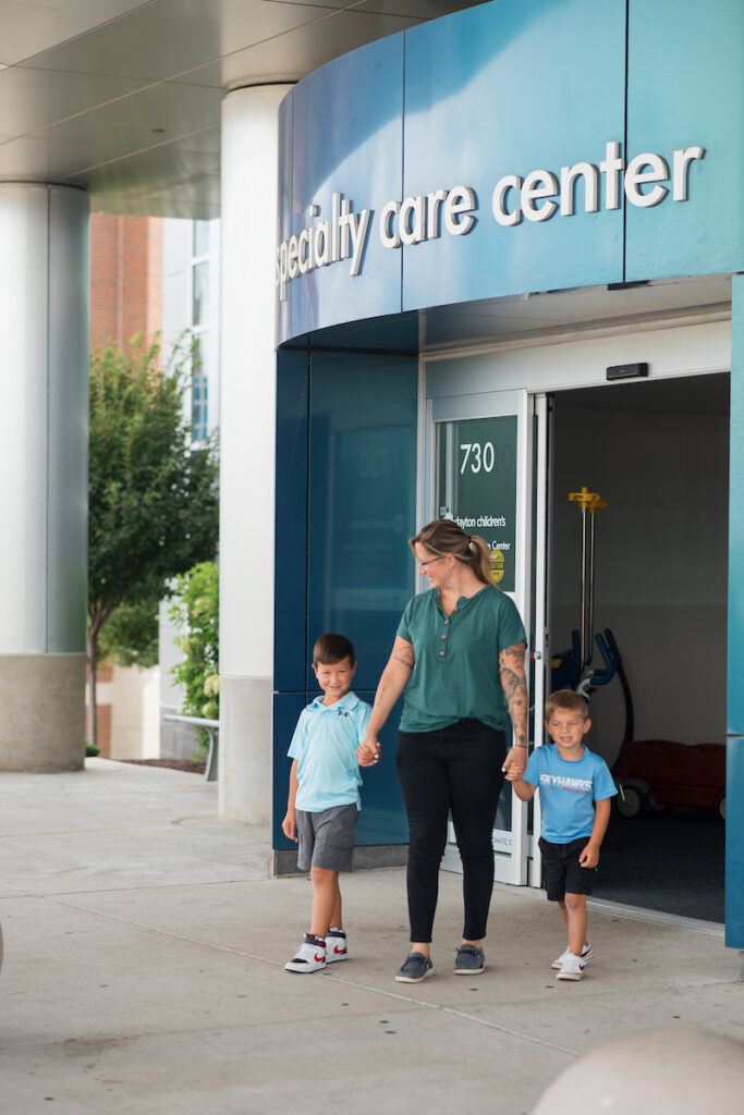 An adult and two young boys walking out of a specialty care center, holding hands and smiling.


