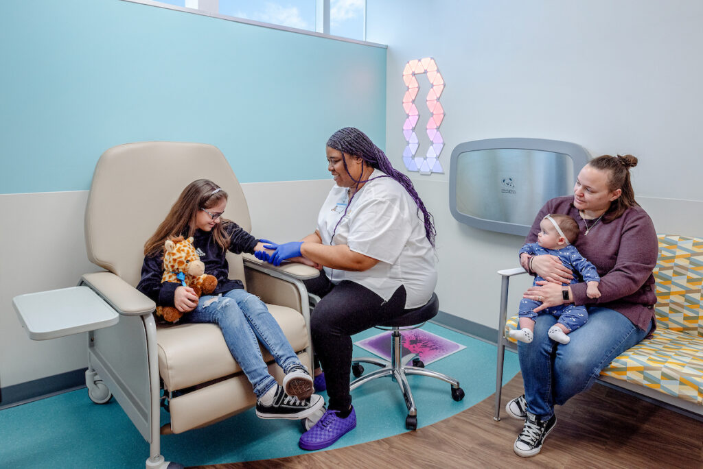 Three laboratory professionals in white coats working and smiling in a medical lab.