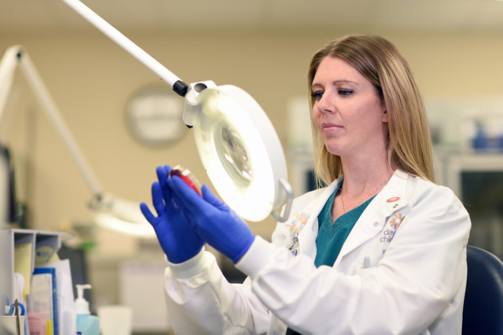 A lab technician studying a sample under a magnifying glass in the Dayton Children’s lab.