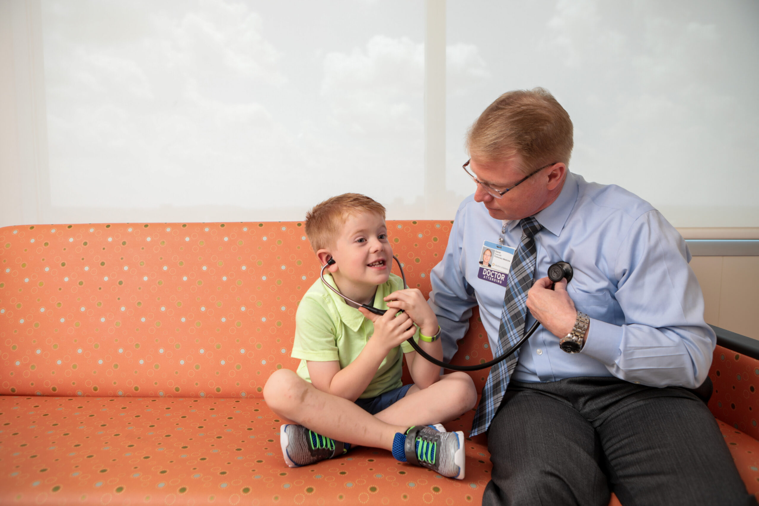 A smiling boy uses a stethoscope to listen to his pulmonary doctor's breathing. 
