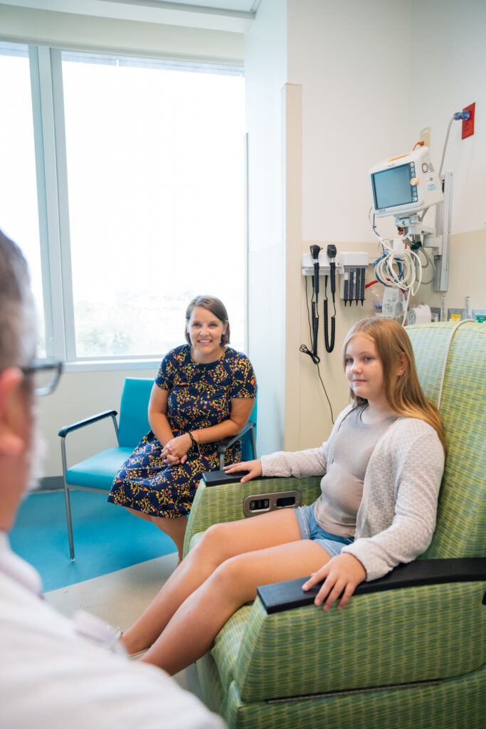 Mom and young patient in an infusion room with a hematology oncology doctor discussing the future of their care.