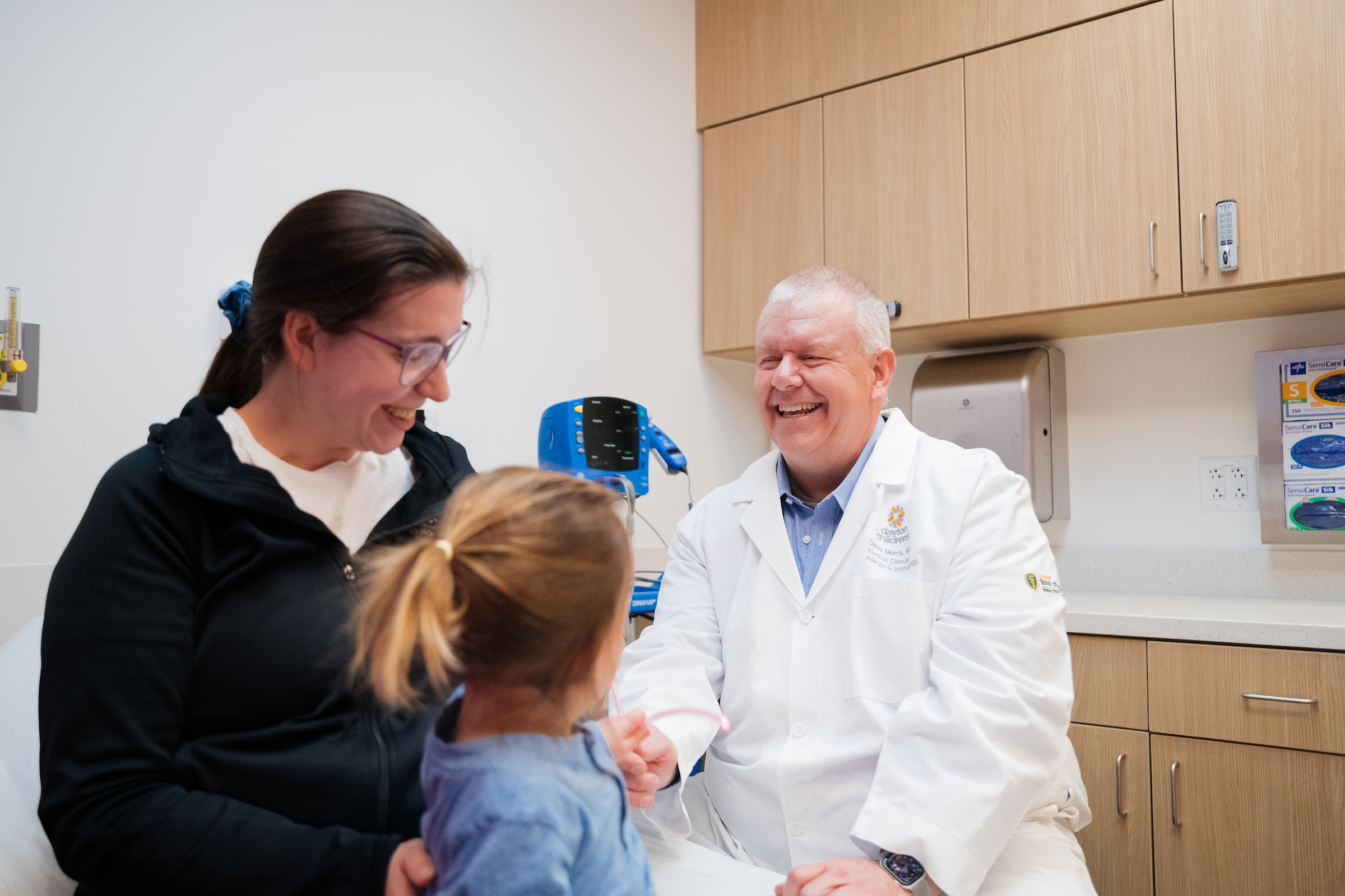 Mom and daughter happily laugh with male doctor during a pediatric allergy and immunology appointment.