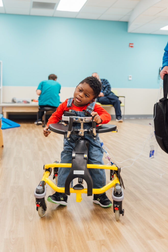 Child participating in a physical therapy session using a yellow gait trainer to practice mobility in a pediatric rehabilitation center.
