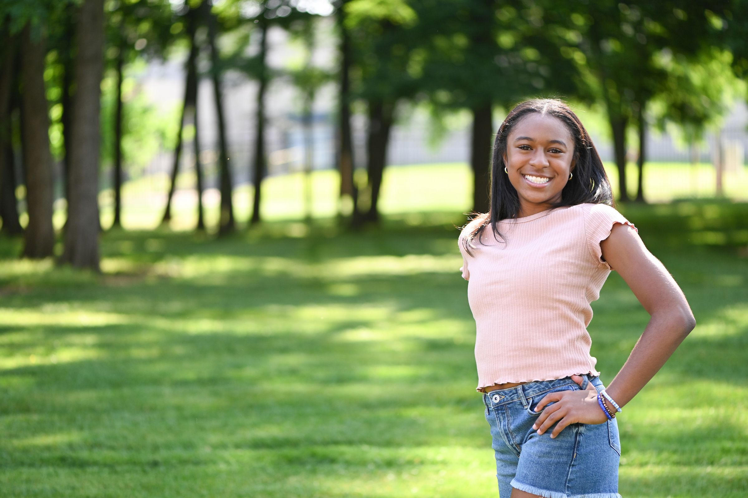 Smiling teenager standing outside in a park, representing strength after completing pediatric physical therapy.

