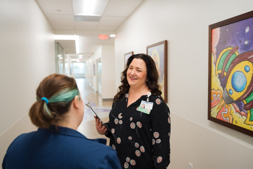 A pediatric neurologist chats with a parent in the hallway of the neurology clinic, helping comfort and answer any questions they have.