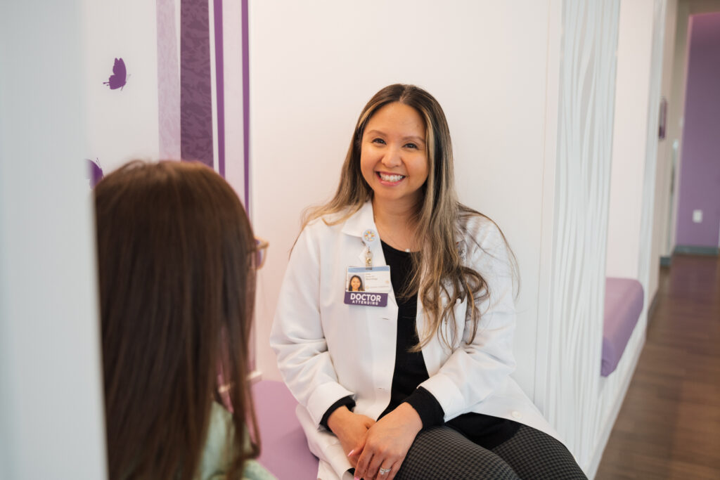 A pediatric neurologist smiles and chats with a patient about neurology conditions and symptoms.