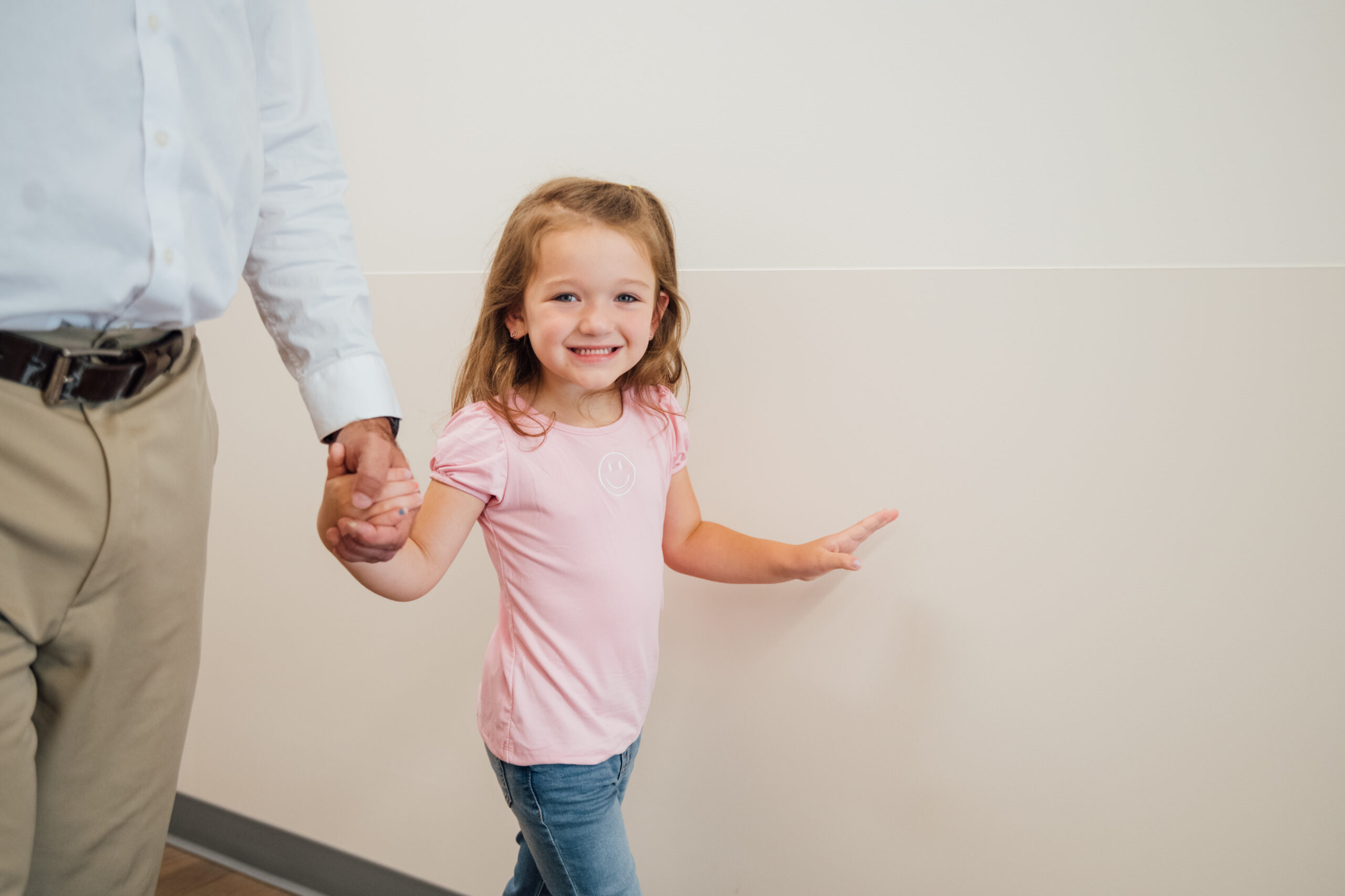 Little girl smiling at the camera, while walking down a clinic hallway.

