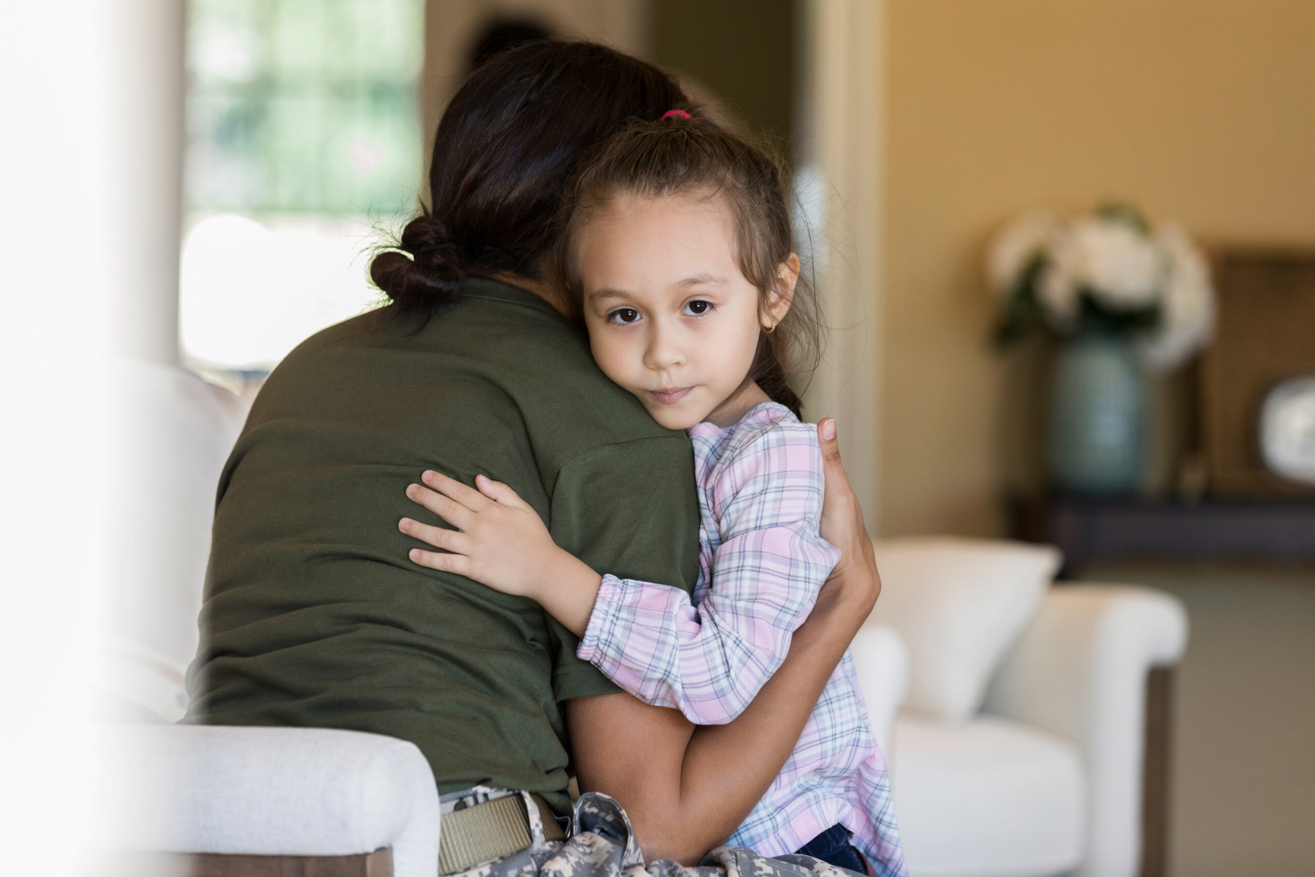 Little girl looking at the camera, hugging her mom.
