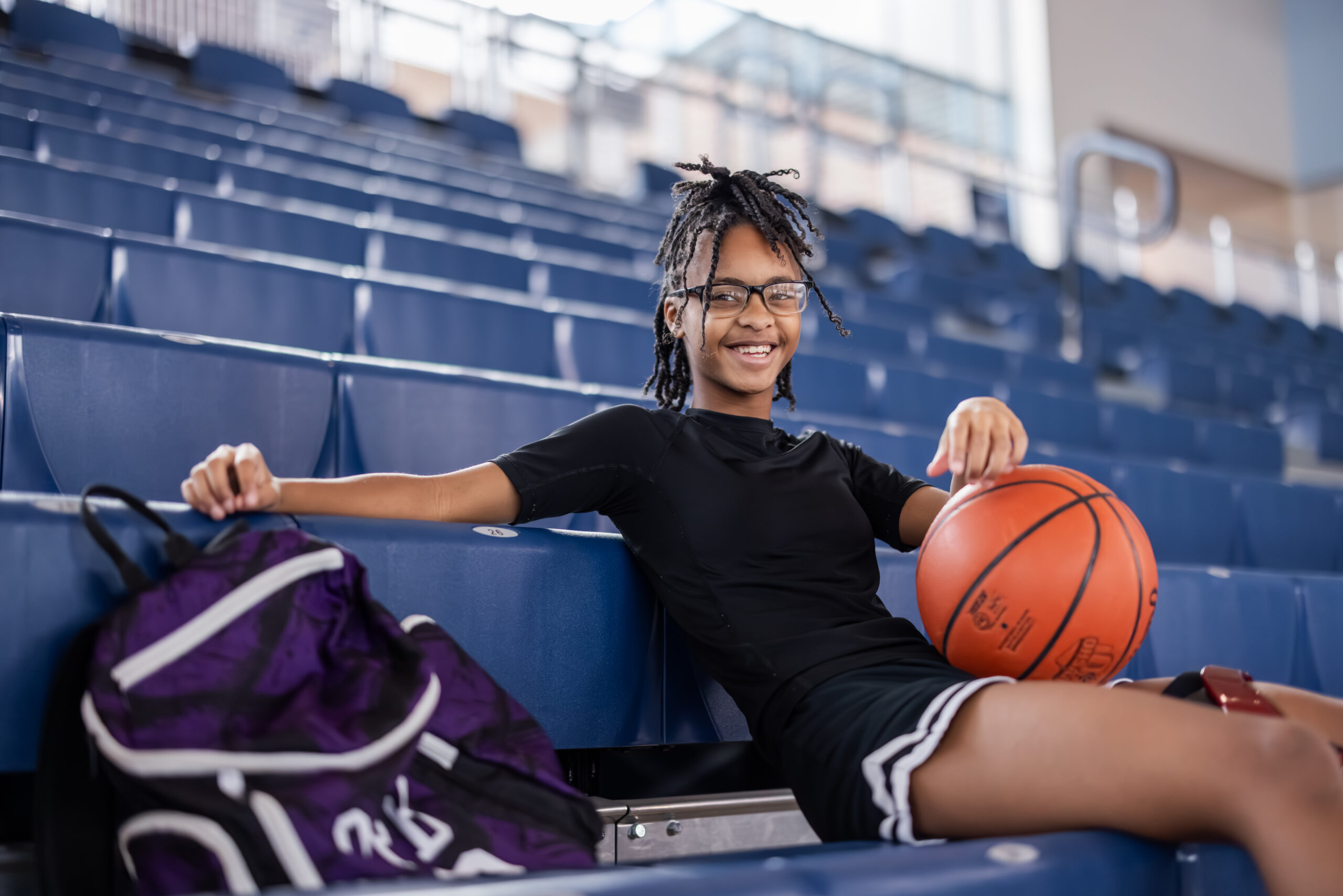 Teen female athlete poses with basketball in gymnasium.