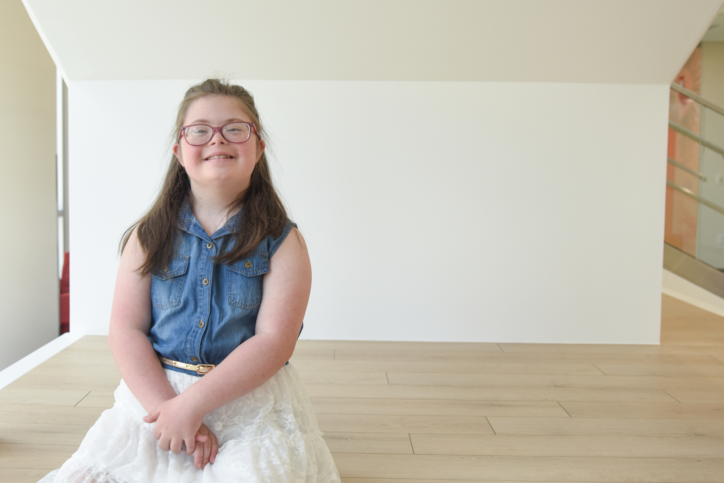 Young girl with glasses, smiles in bright lobby area waiting for her pediatric cardiology appointment